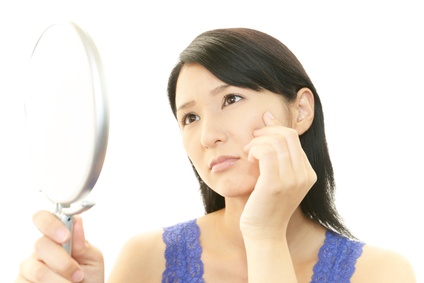 鏡を見て顔のシミやたるみを気にする女性