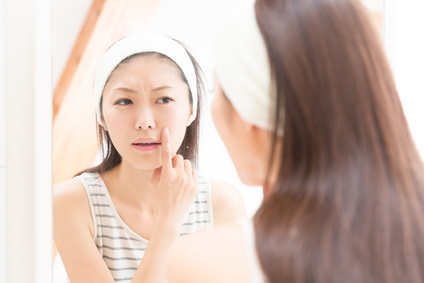 洗面台の鏡で突っ張った肌を確認する女性